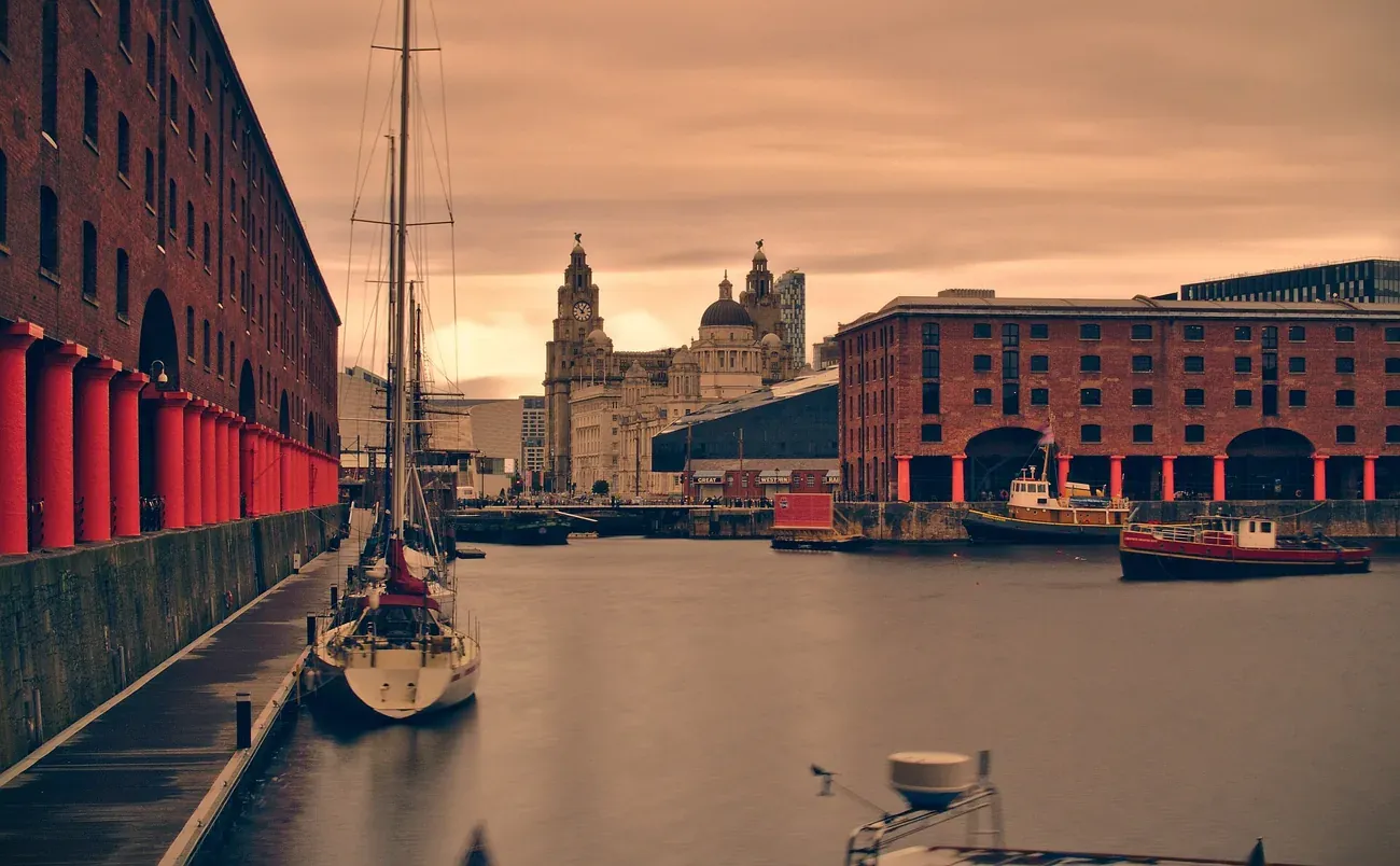 The Royal Albert Dock colonnade and a moored sailboat at sunset with the Royal Liver Building behind, Liverpool