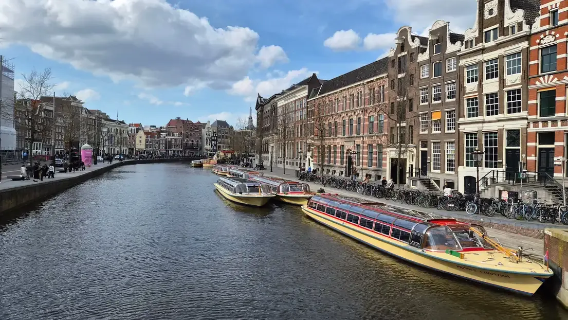 Tour boats moored along an Amsterdam canal lined with historic houses