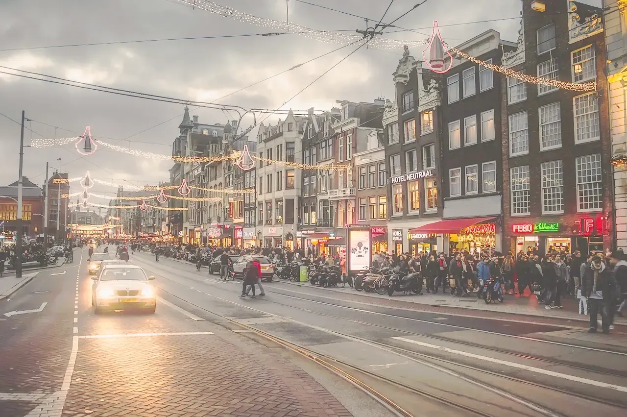 Christmas lights hanging over a busy shopping street in Amsterdam at dusk