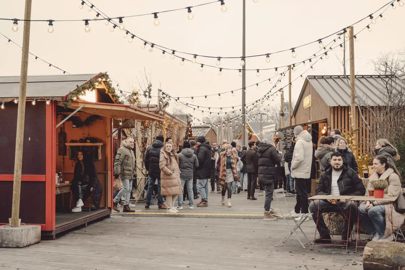 Visitors at a winter market with wooden stalls under string lights