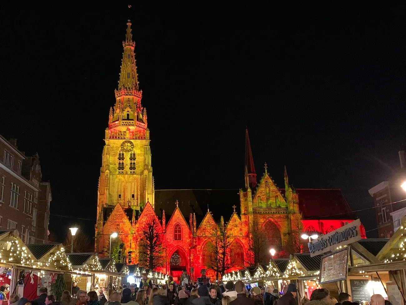 Lit chalets of the Christmas market in Anderlecht in front of the illuminated collegiate church of Saints Peter and Guido