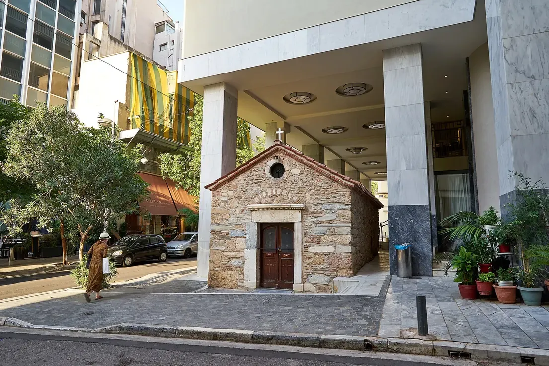 The small stone chapel of Agia Dynamis standing under the raised marble pillars of a 1930s building on Mitropoleos Street in Athens