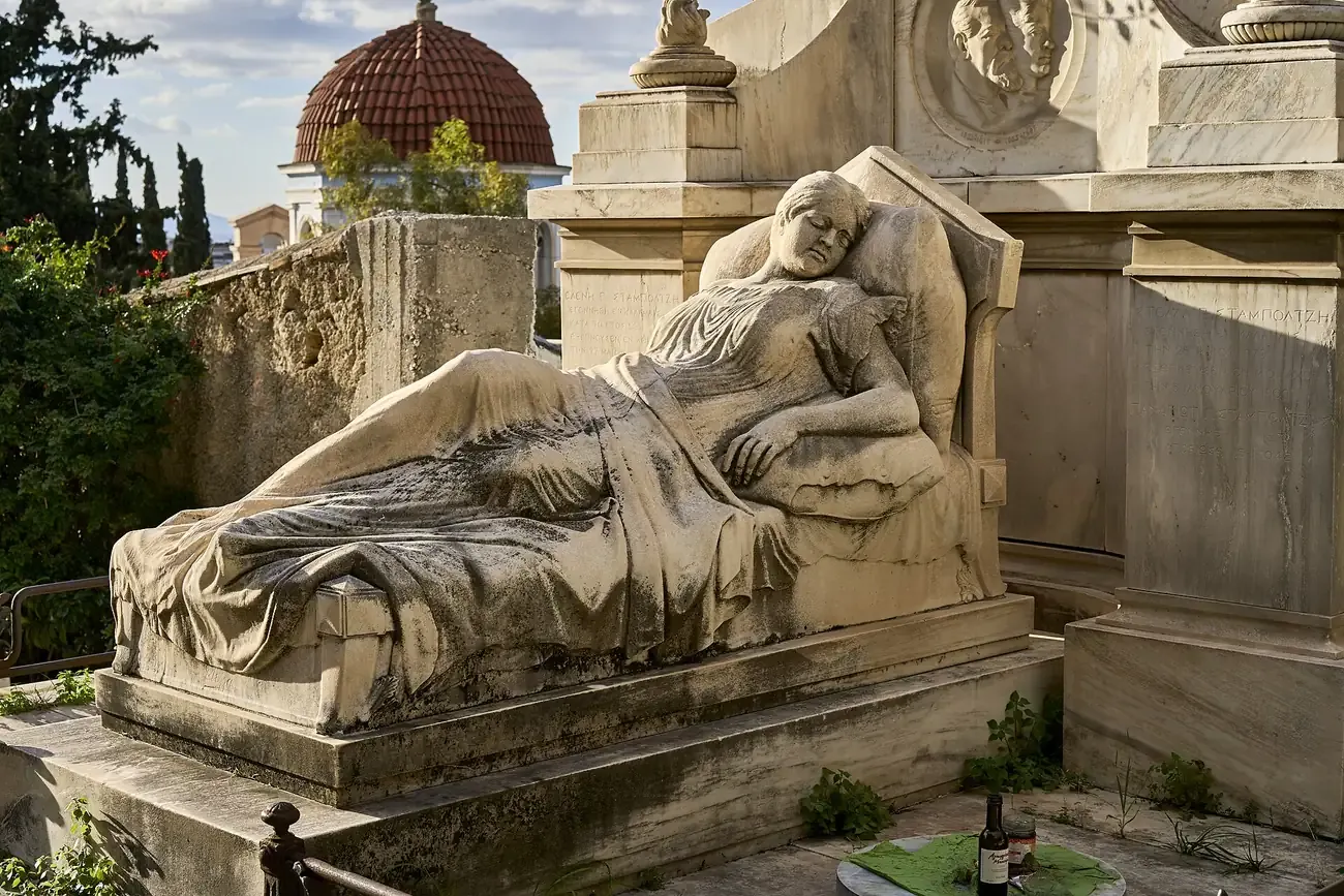 A clothed marble funerary statue on a family tomb among greenery in the First Cemetery of Athens