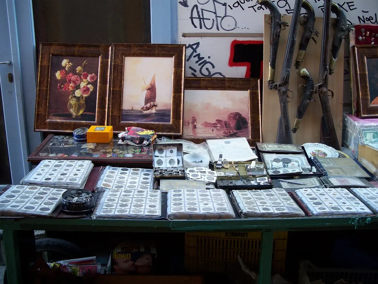 An antiques stall at the Monastiraki flea market in Athens with coins, framed paintings and old flintlock pistols
