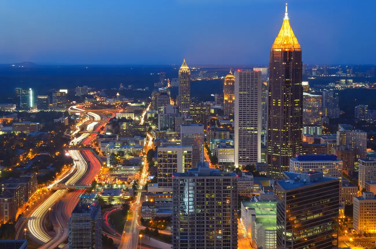Downtown Atlanta towers lit at dusk above the winding lights of the interstate