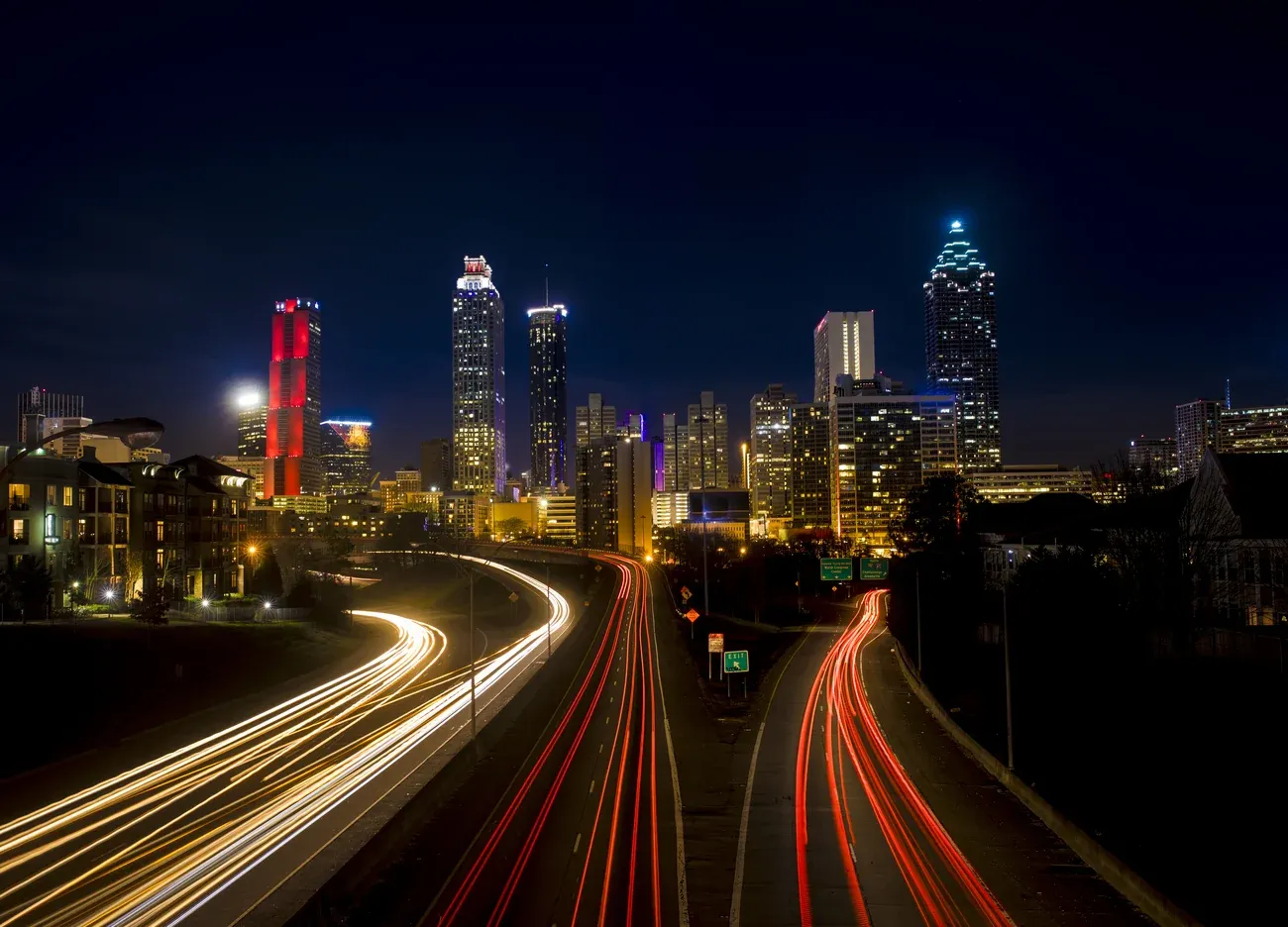 Light trails of traffic on the freeway leading into the lit Atlanta skyline at night