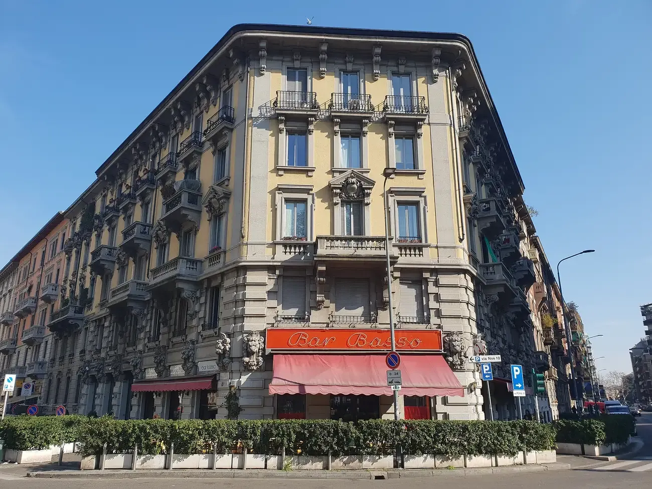 The corner facade of Bar Basso with its orange sign and red awning on Via Plinio in Milan