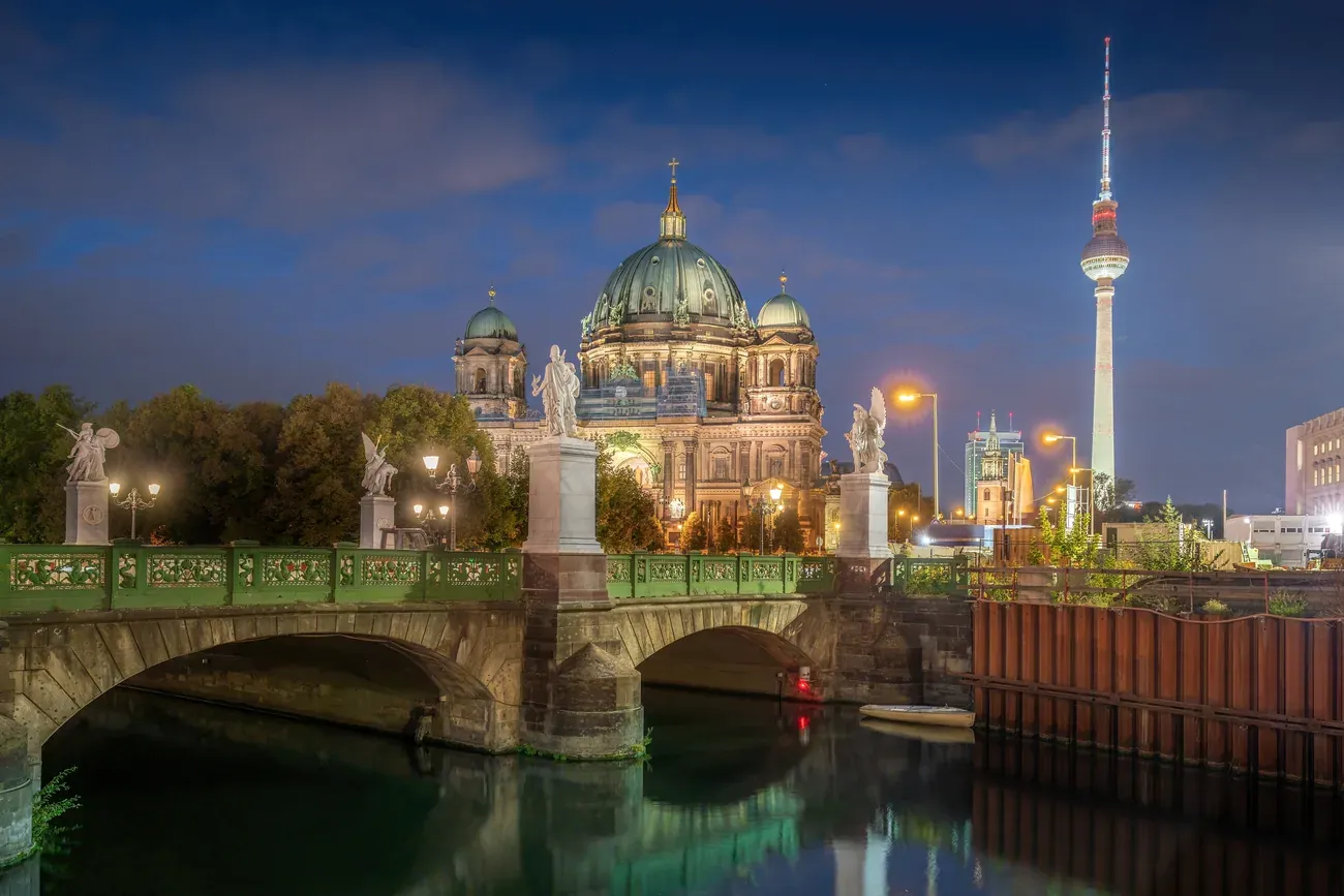 Berlin Cathedral lit at night beyond the Schlossbruecke over the Spree, with the TV Tower behind