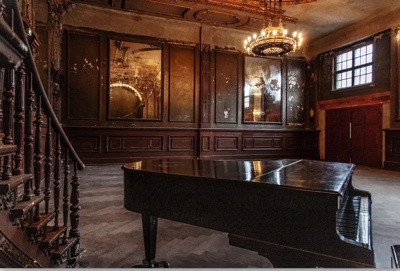 Cracked antique mirror panels, a chandelier and a grand piano inside the Spiegelsaal above Clarchens Ballhaus in Berlin