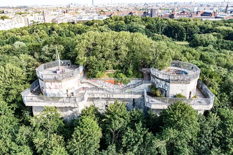 Aerial view of the two wartime flak tower stumps of Flakturm Humboldthain rising above the trees of Volkspark Humboldthain, with the Berlin skyline behind