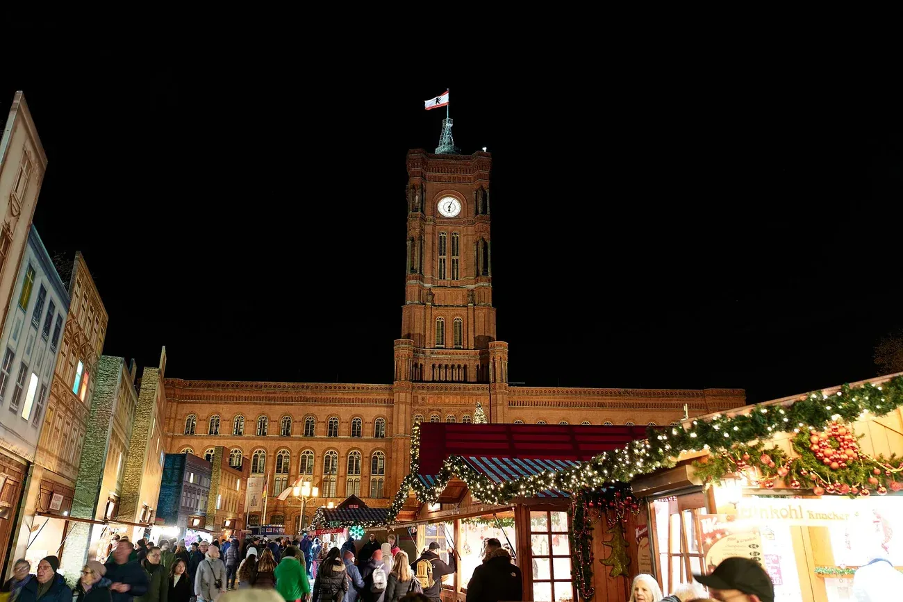 The clock tower of the Rotes Rathaus above the lit stalls of the Berliner Weihnachtszeit at night