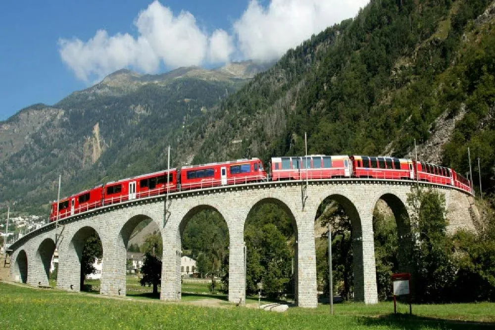 Bernina Express train climbing the stone spiral viaduct of Brusio in a green valley