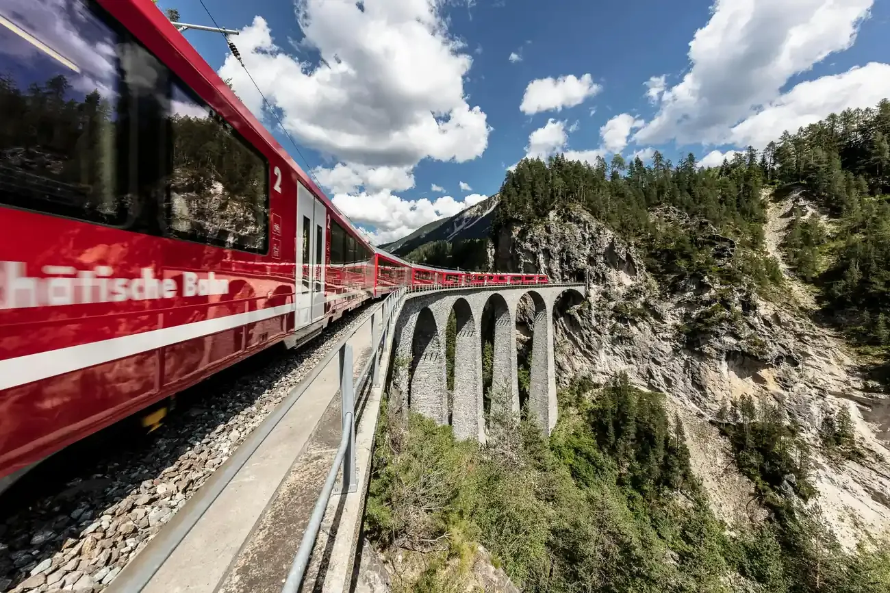 Red Bernina line train crossing a curved stone viaduct on a rocky Alpine mountainside