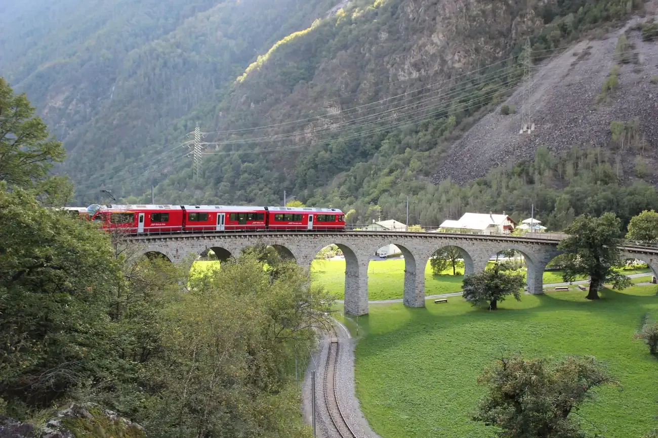 Red Bernina regional train on the Brusio spiral viaduct surrounded by trees and meadows