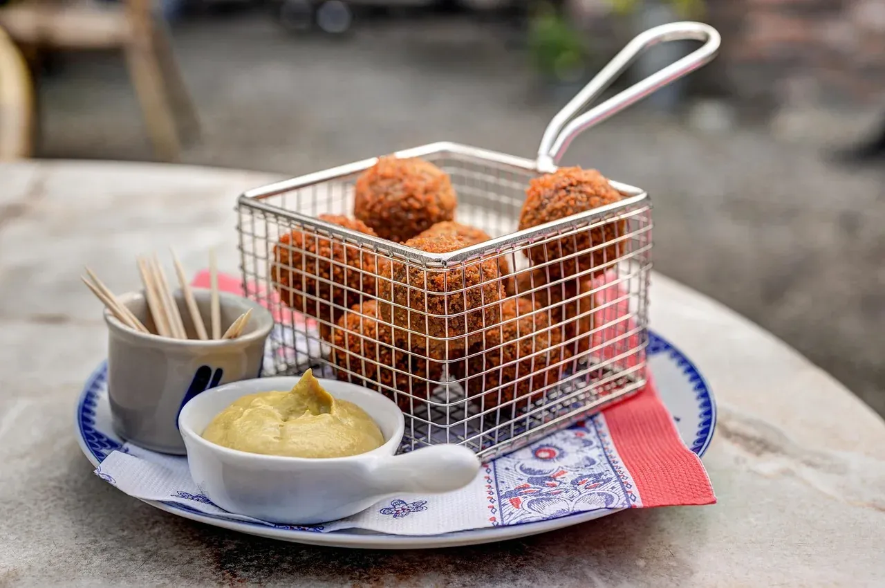 Bitterballen served in a wire basket with a dish of mustard on a Delft blue plate