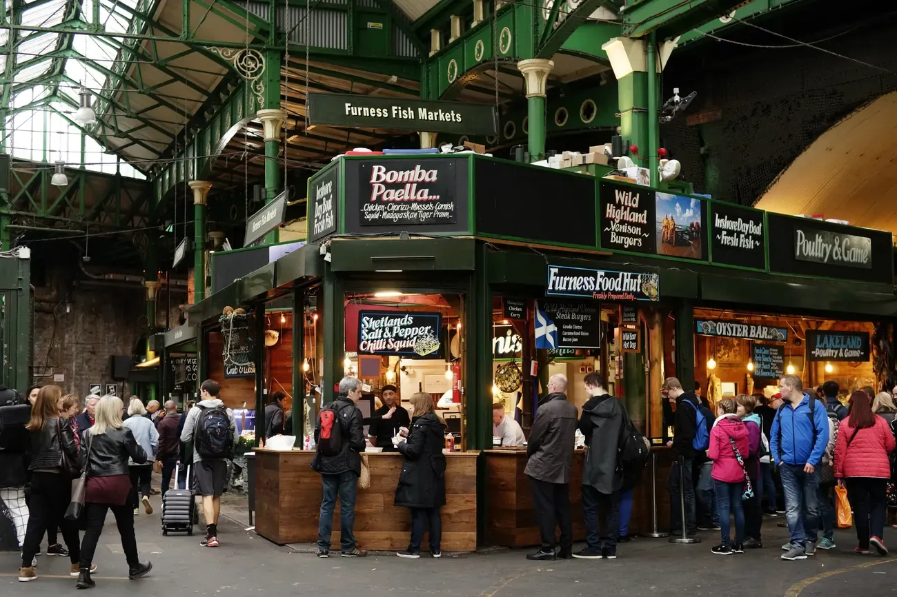 Shoppers at food stalls under the green iron roof of Borough Market in London