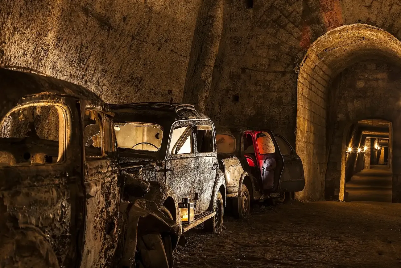 Rusting vintage cars parked along a tuff-walled passage of the Bourbon Tunnel in Naples