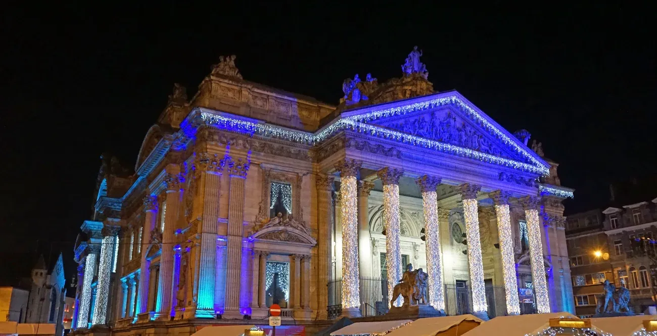 The former stock exchange on the Place de la Bourse in Brussels lit in blue at night, with Christmas market chalets in front