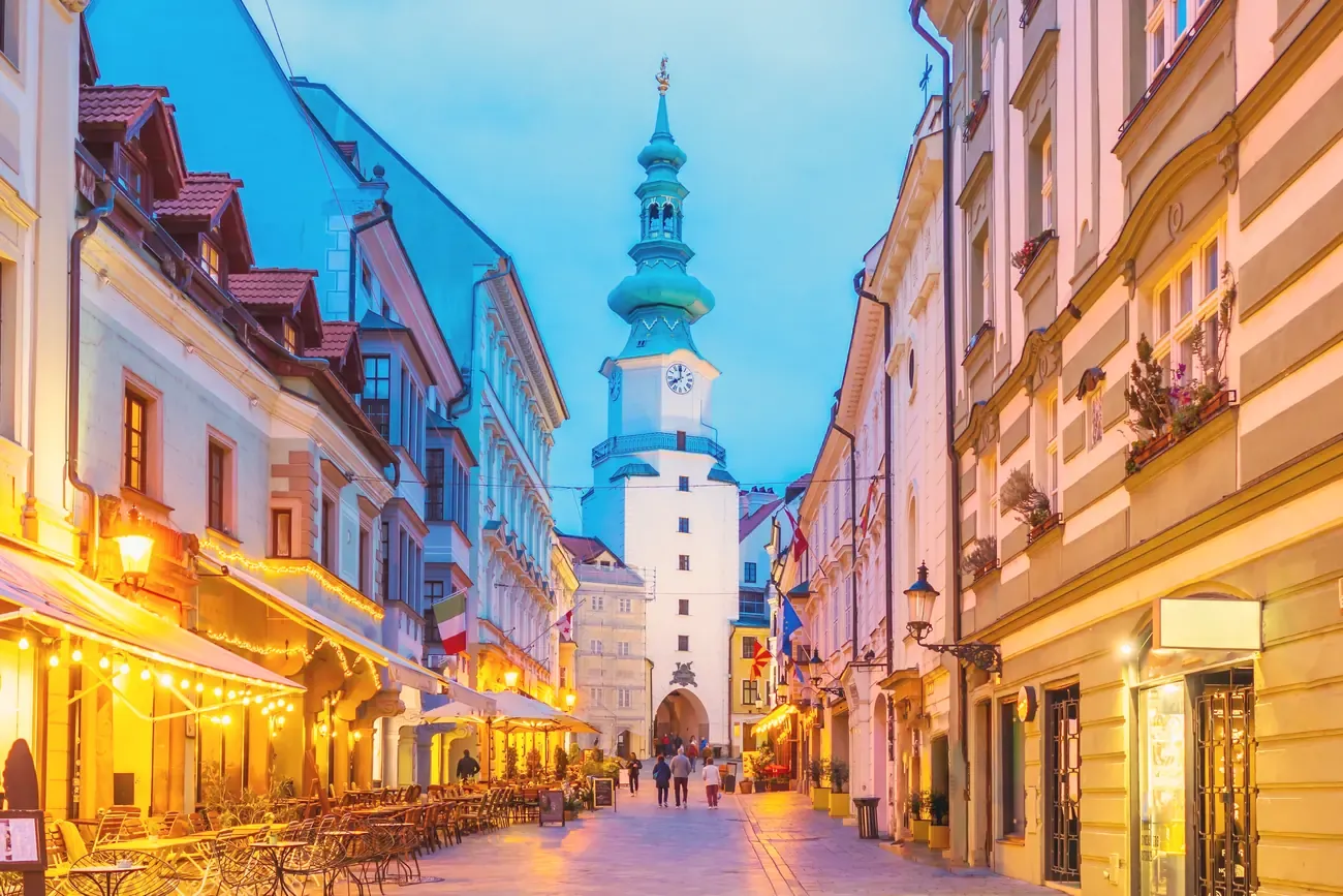 Michael's Gate tower lit above a cafe-lined street in Bratislava's old town at dusk