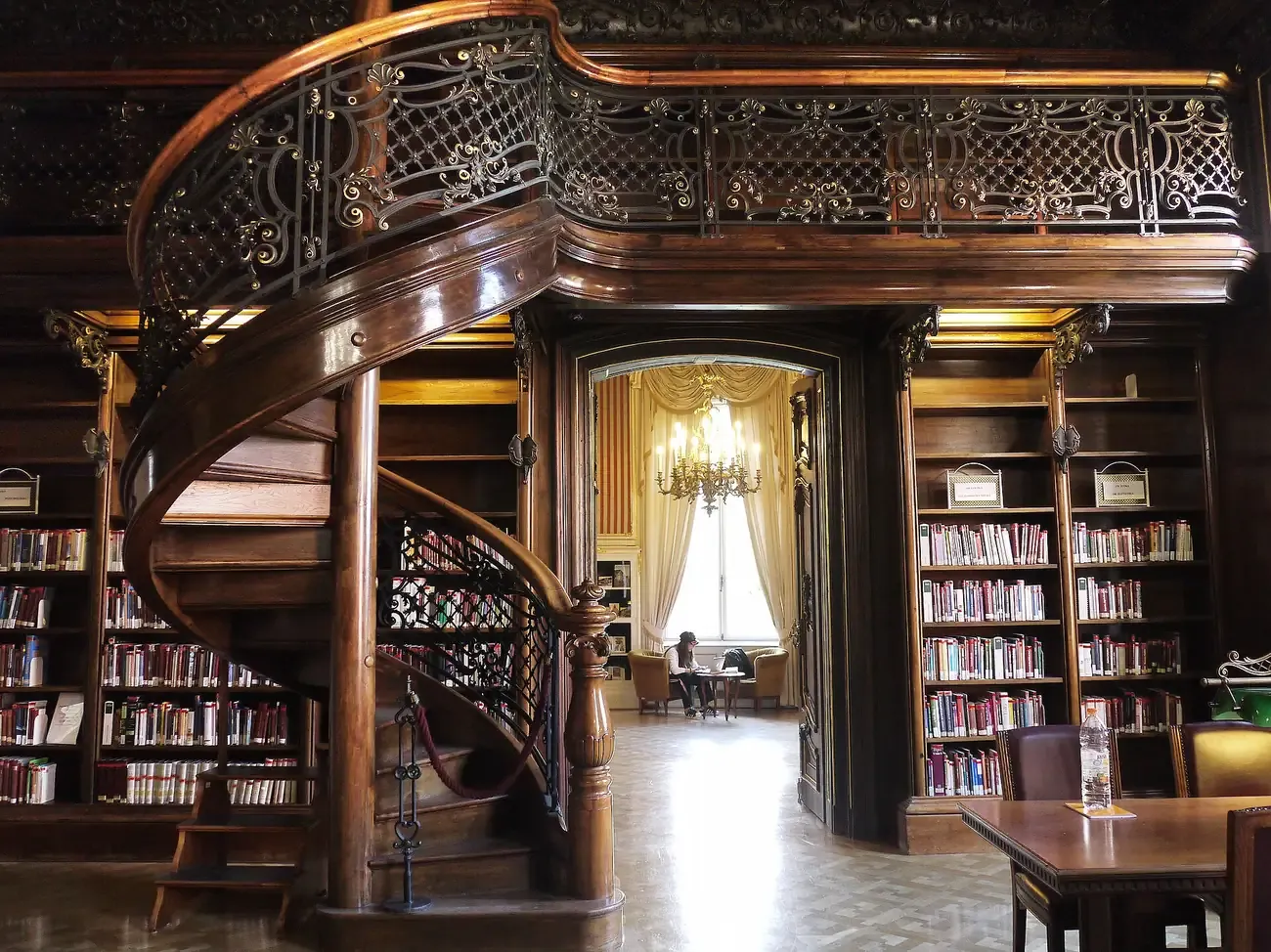 The oak-panelled reading room of the Szabo Ervin Library in Budapest with a carved spiral staircase, wrought-iron gallery and chandelier