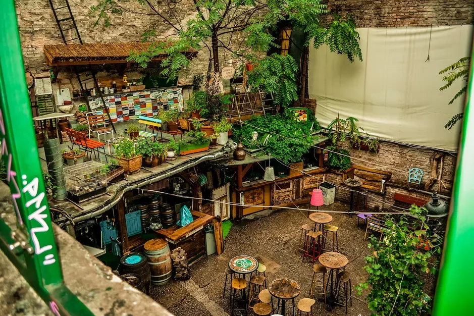 The empty open-air courtyard of Szimpla Kert ruin bar in Budapest with mismatched tables, stools and salvaged furniture among plants