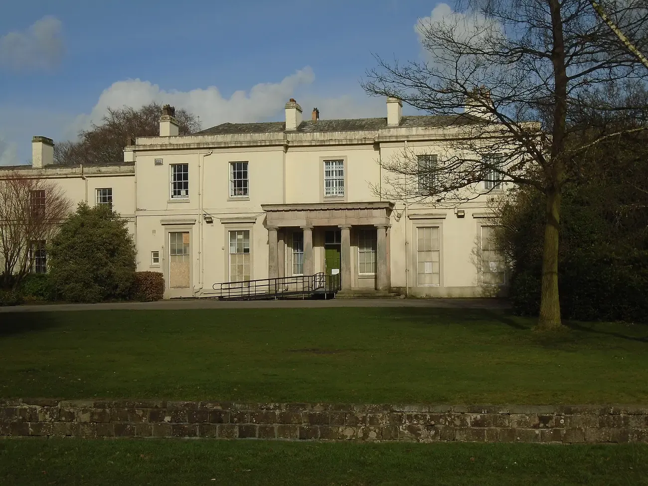 The white front of Calderstones Mansion House in Calderstones Park, Liverpool, with a lawn and bare trees