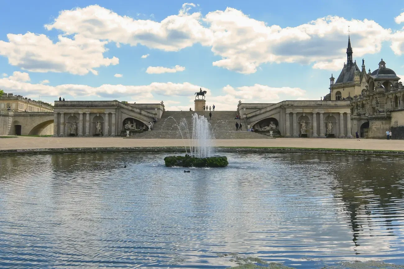 Chateau de Chantilly viewed across its fountain and moat on a sunny day, France