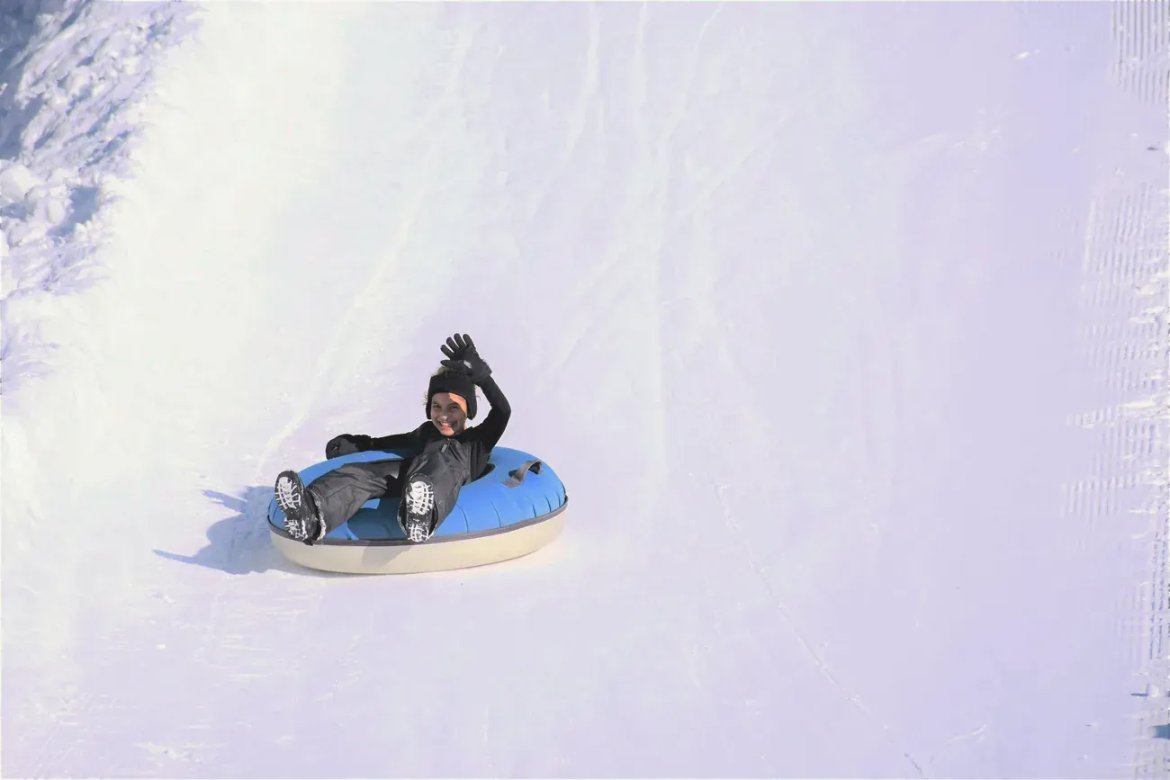 Child waving while sliding down a snowy slope on a rubber tube
