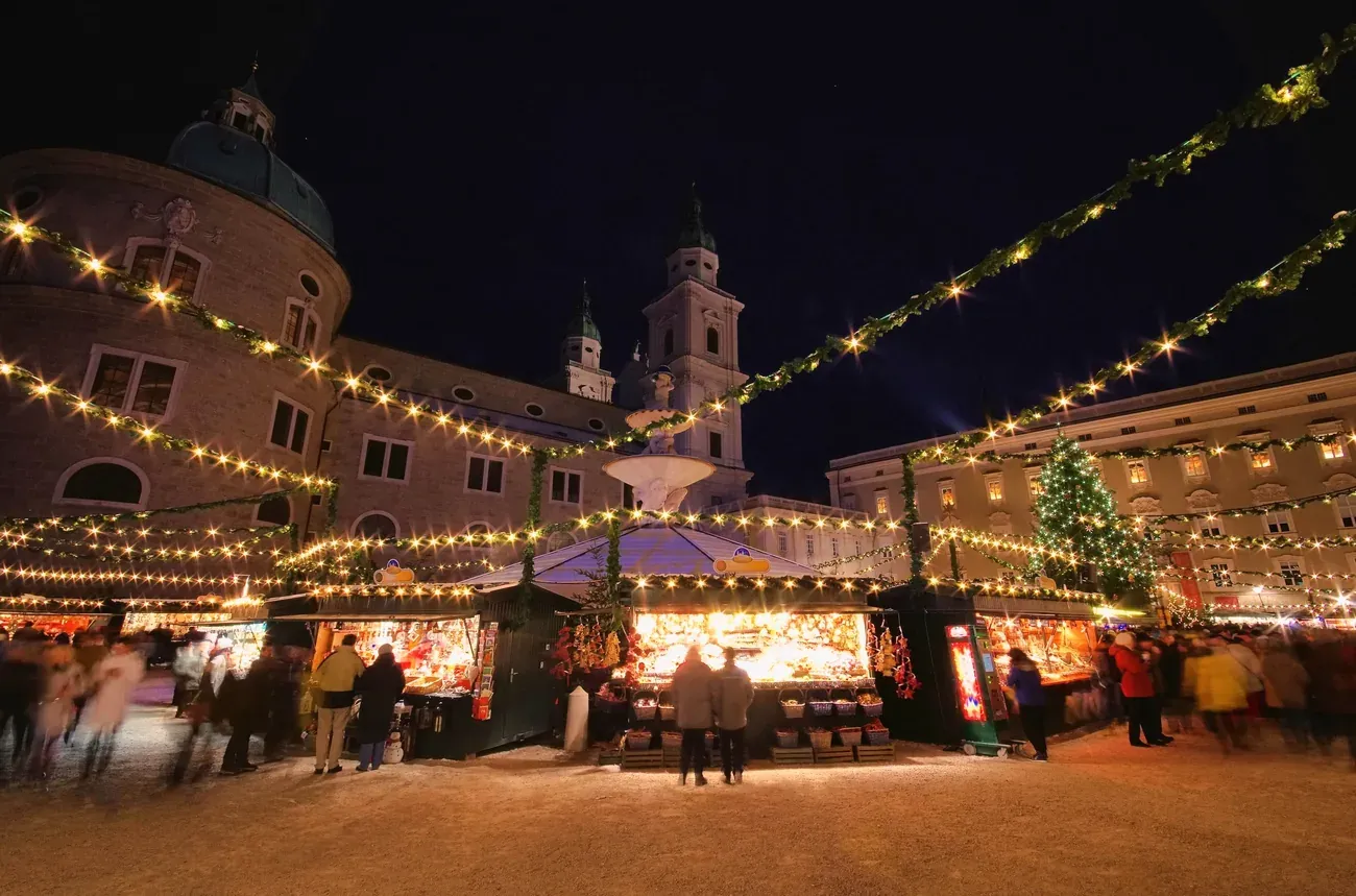 Stalls of the Christkindlmarkt on Domplatz in Salzburg at night, with the cathedral behind