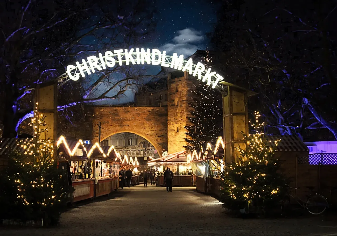 The lit Christkindlmarkt arch and stalls in front of the Sendlinger Tor gate at night, Munich