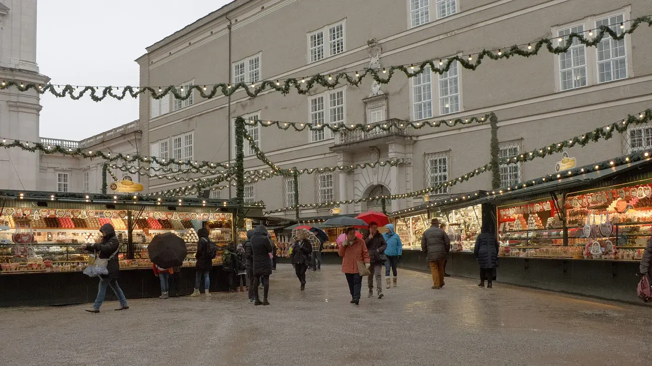 Stalls of the Christkindlmarkt on Domplatz in Salzburg in daylight, with garlands strung across the square