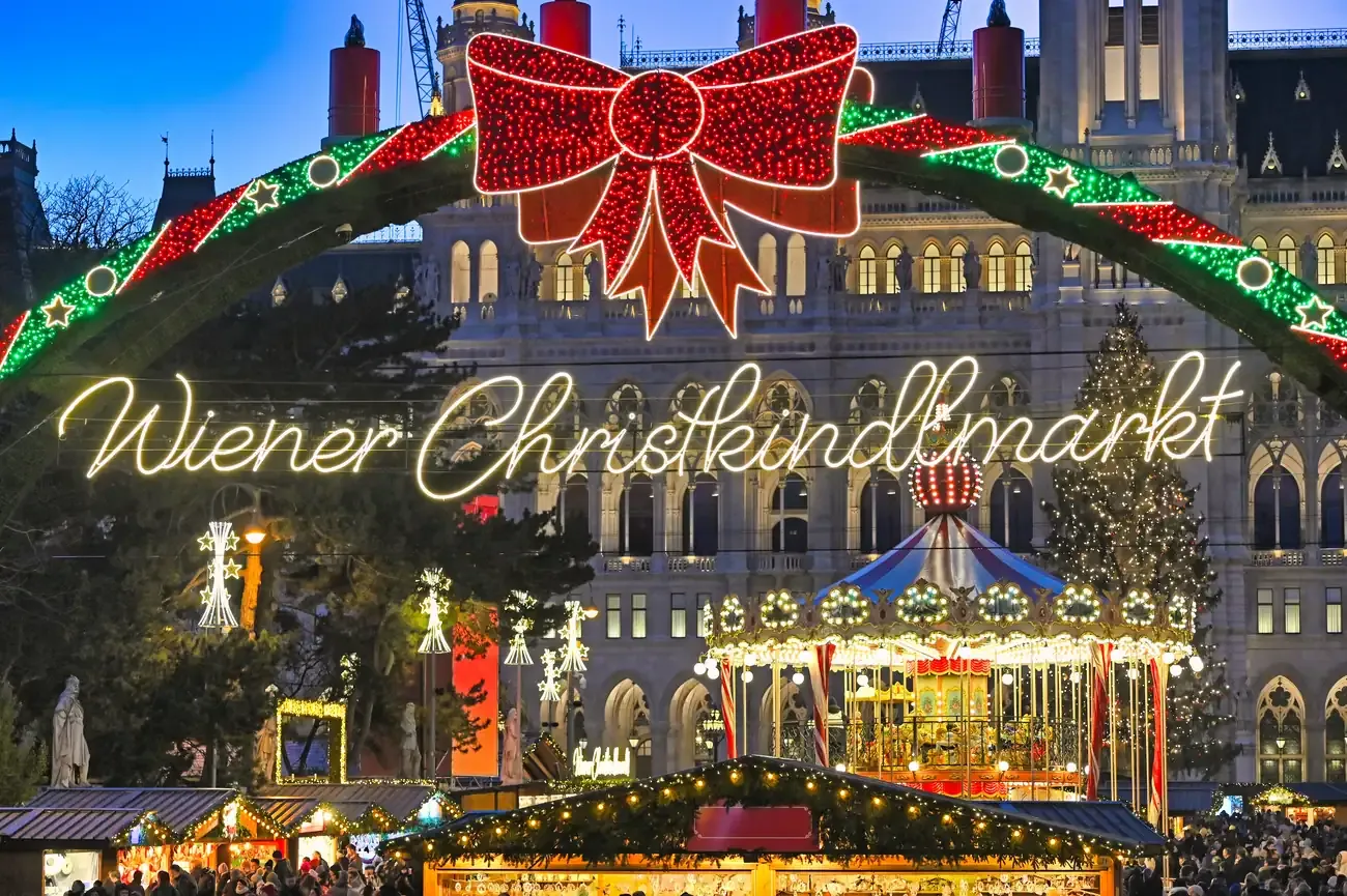 Carousel and stalls of the Christmas market on Rathausplatz under the Wiener Christkindlmarkt arch, Vienna