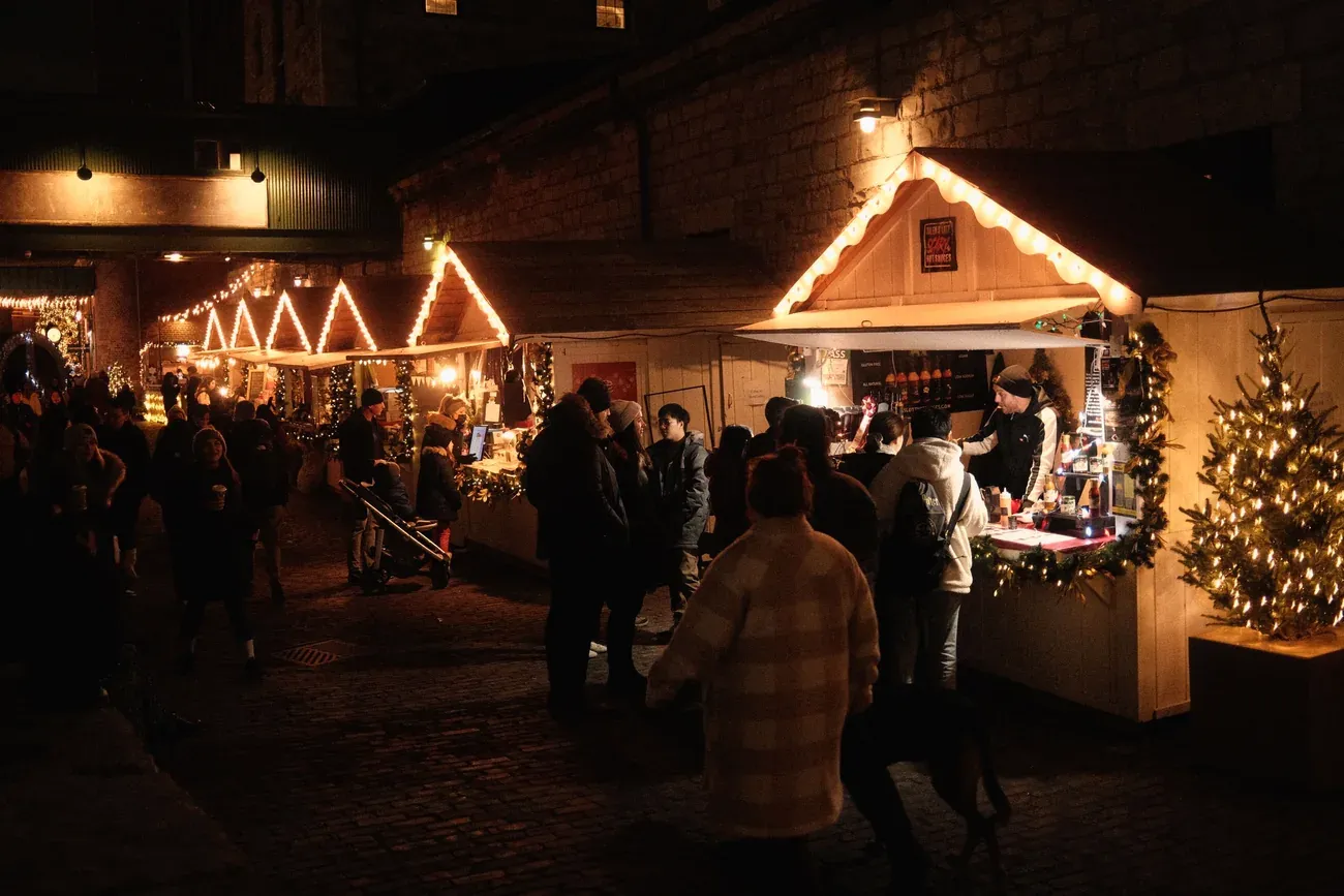 Visitors walking between lit wooden Christmas market chalets at night