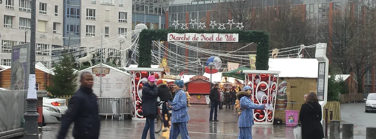 The entrance arch of the Christmas market on Place Rihour in Lille, with chalets and visitors on the square