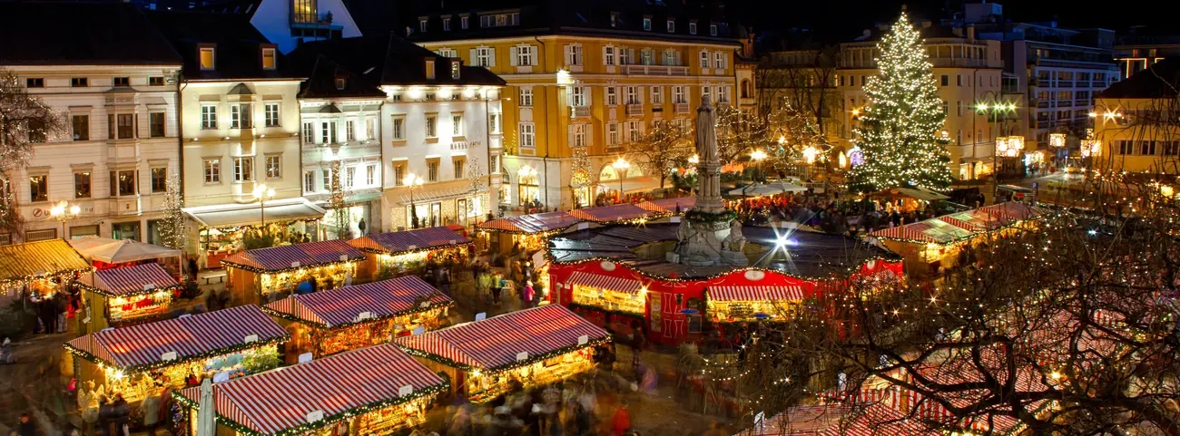 The Christmas market on Piazza Walther in Bolzano seen from above at dusk, with the lit tree and the Walther monument
