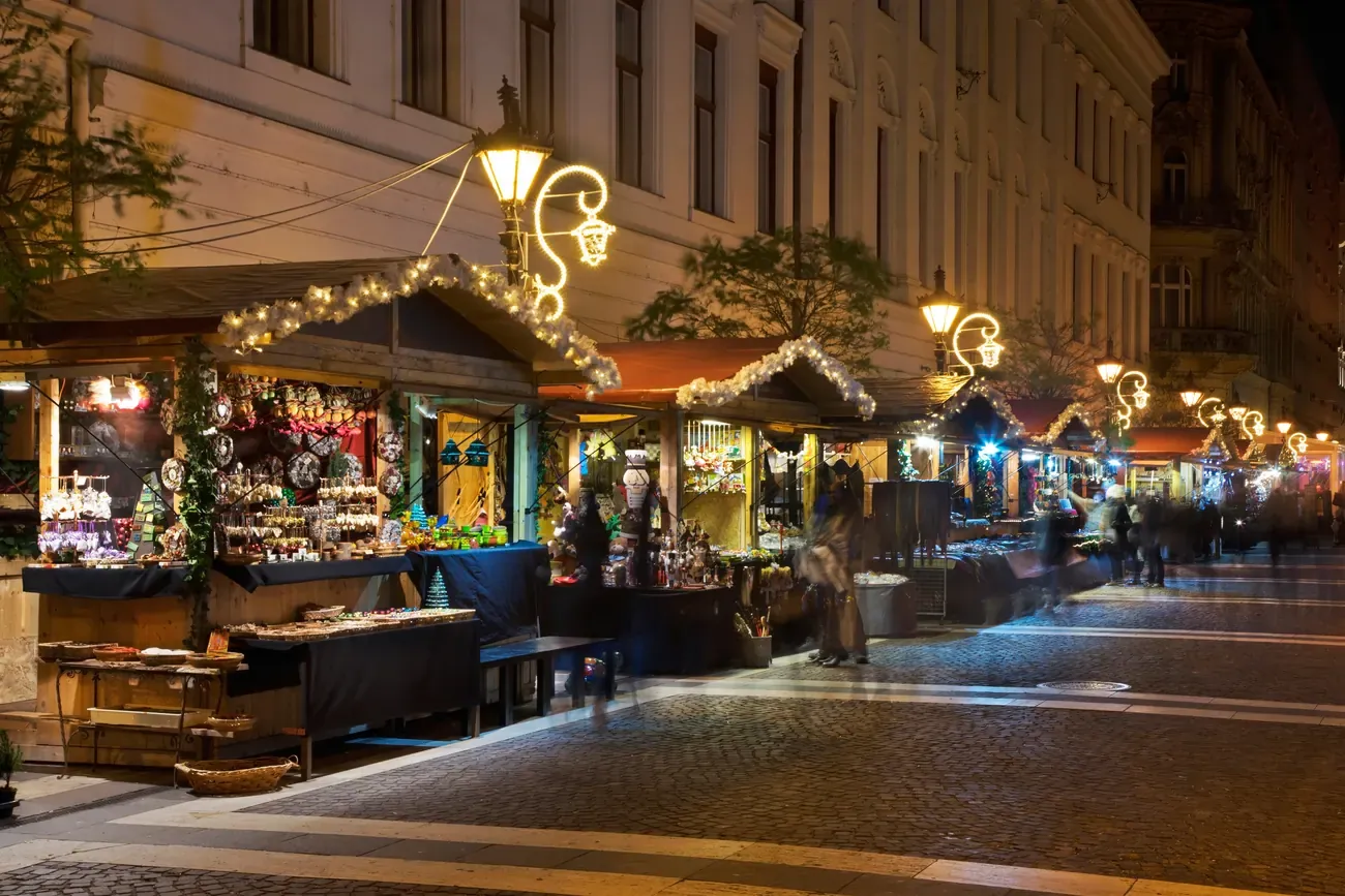 Lit Christmas market stalls and street lamps decorated with garlands on a street in central Budapest in the evening