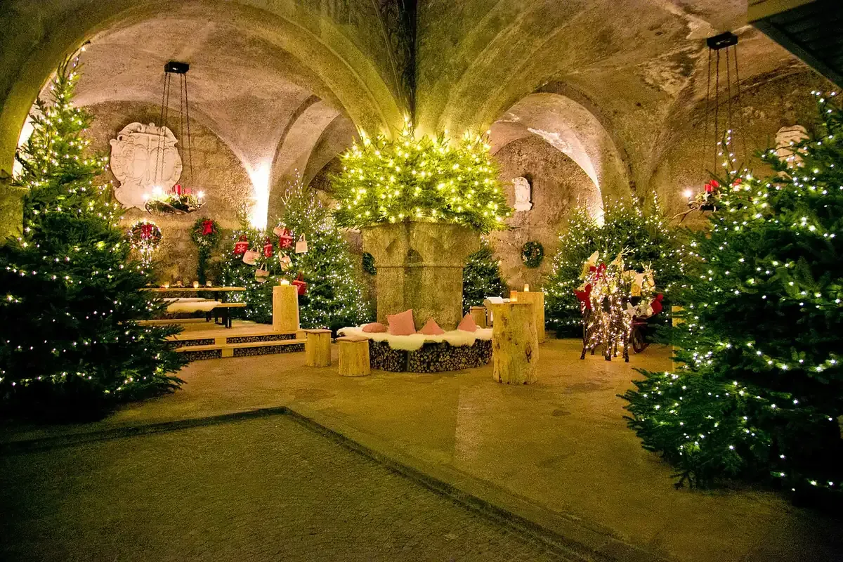 Lit Christmas trees in the vaulted arcade courtyard of the St. Peter Stiftskulinarium in Salzburg