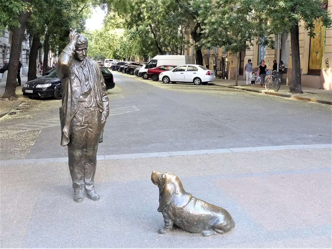 Bronze statue of Columbo scratching his head with his basset hound at his feet on a street corner in Budapest