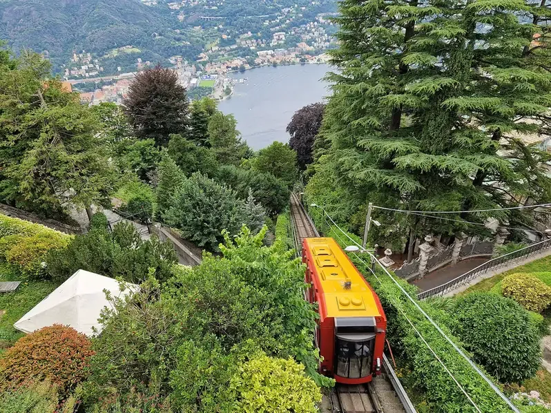 A Como-Brunate funicular car descending through gardens with Como and the lake below