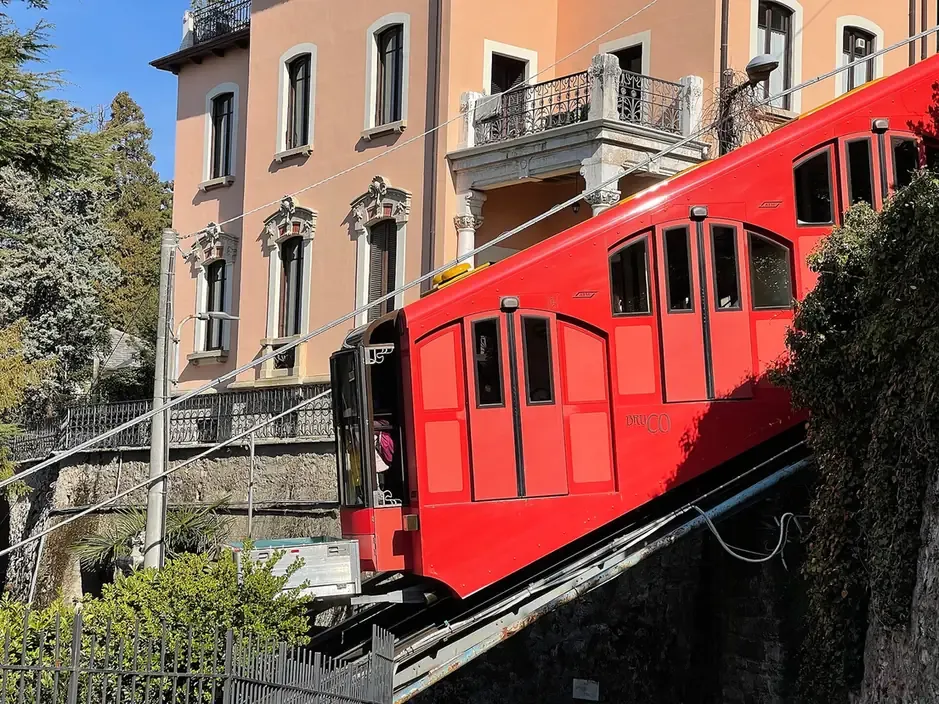 A red Como-Brunate funicular car climbing past a villa near the upper station