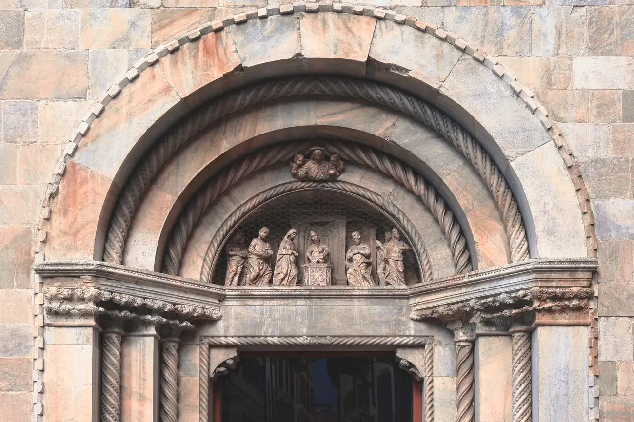 Carved figures in the arched lunette over a portal of Como Cathedral