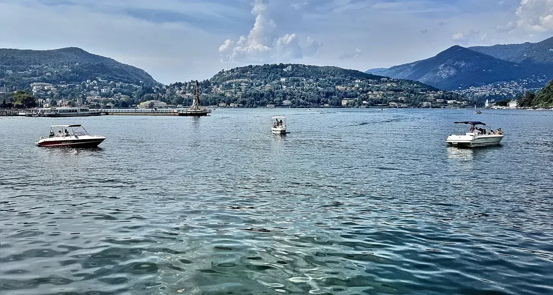 Motorboats on the first basin of Lake Como in front of the Diga Foranea pier, with the hillside of Como behind