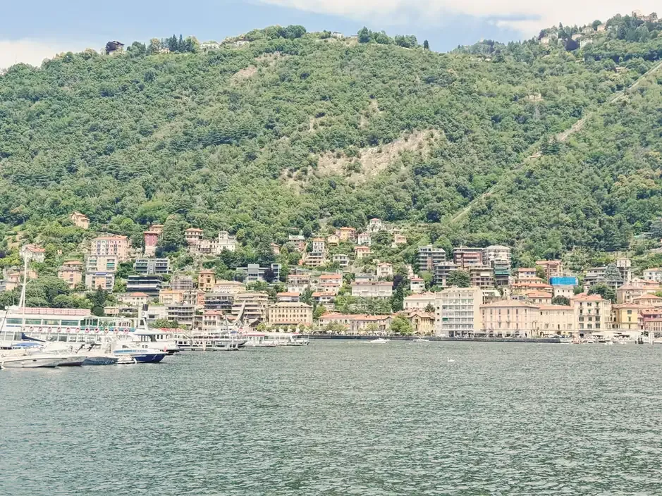 Ferries and boats in the harbour of Como below the wooded Brunate hill