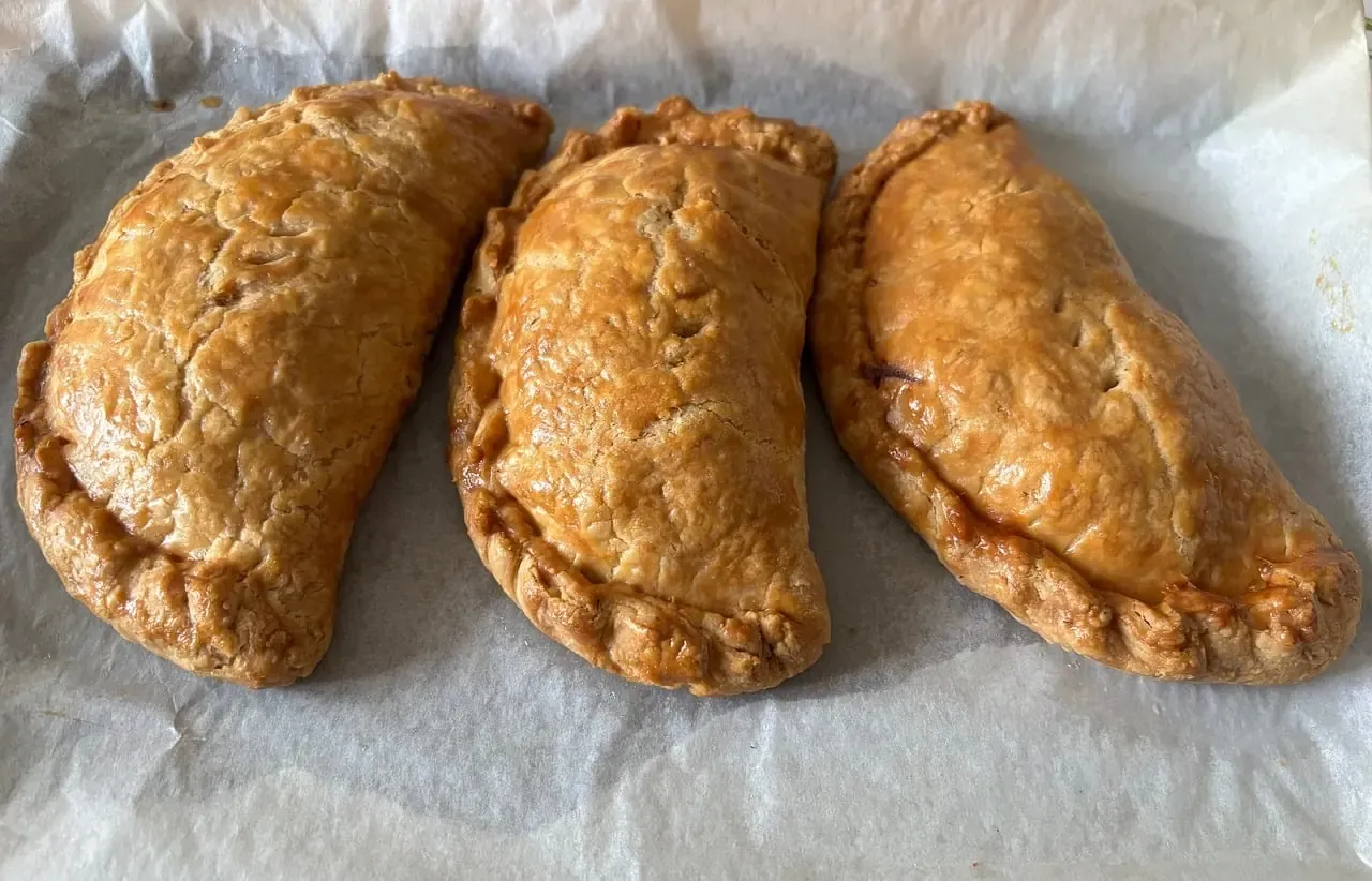Three baked Cornish pasties resting on baking paper