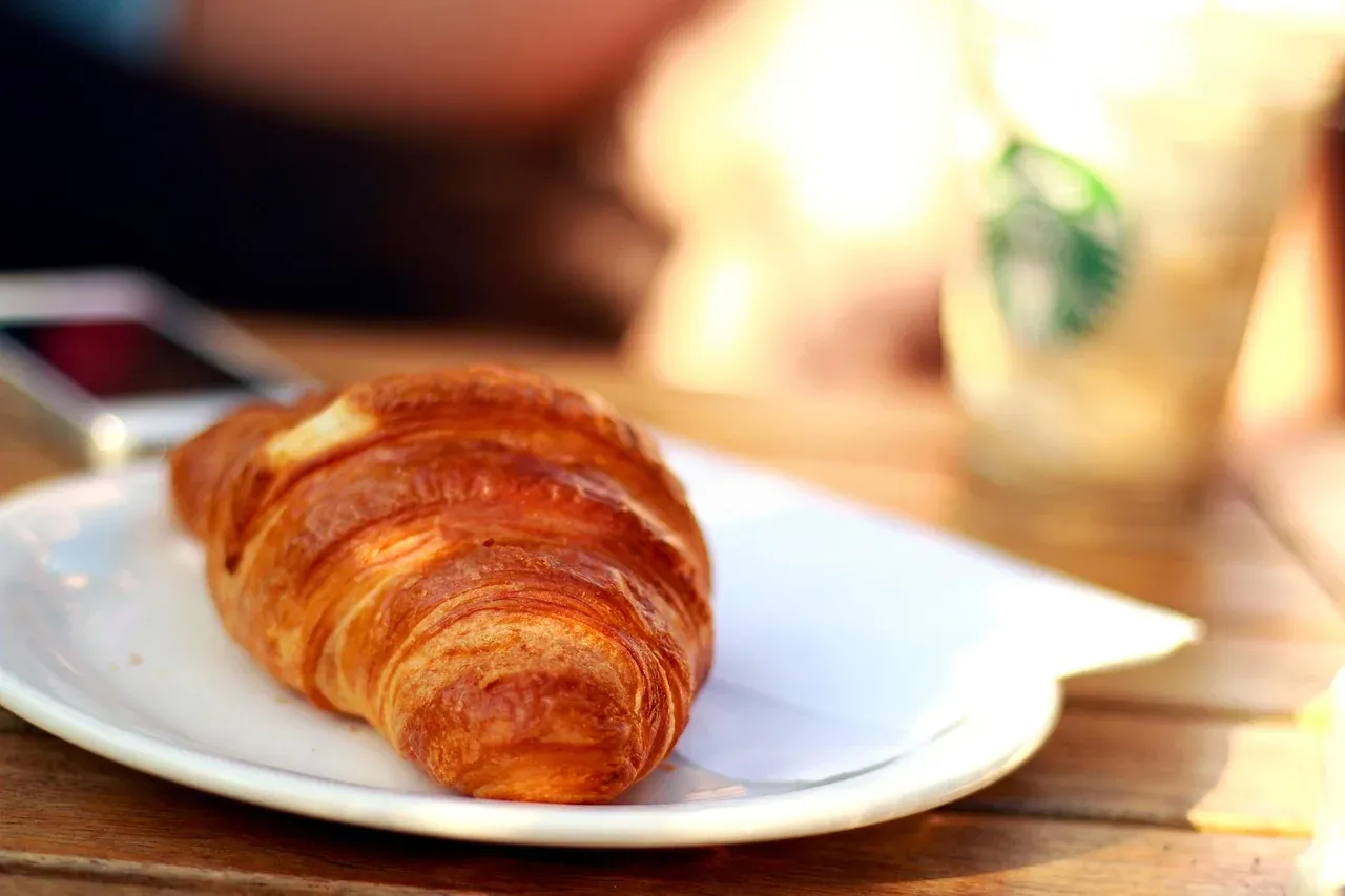 A flaky croissant served on a plate at a French cafe table
