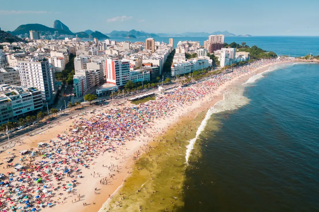 Crowded Ipanema beach packed with sun umbrellas beside the Arpoador headland on a sunny day, Rio de Janeiro.