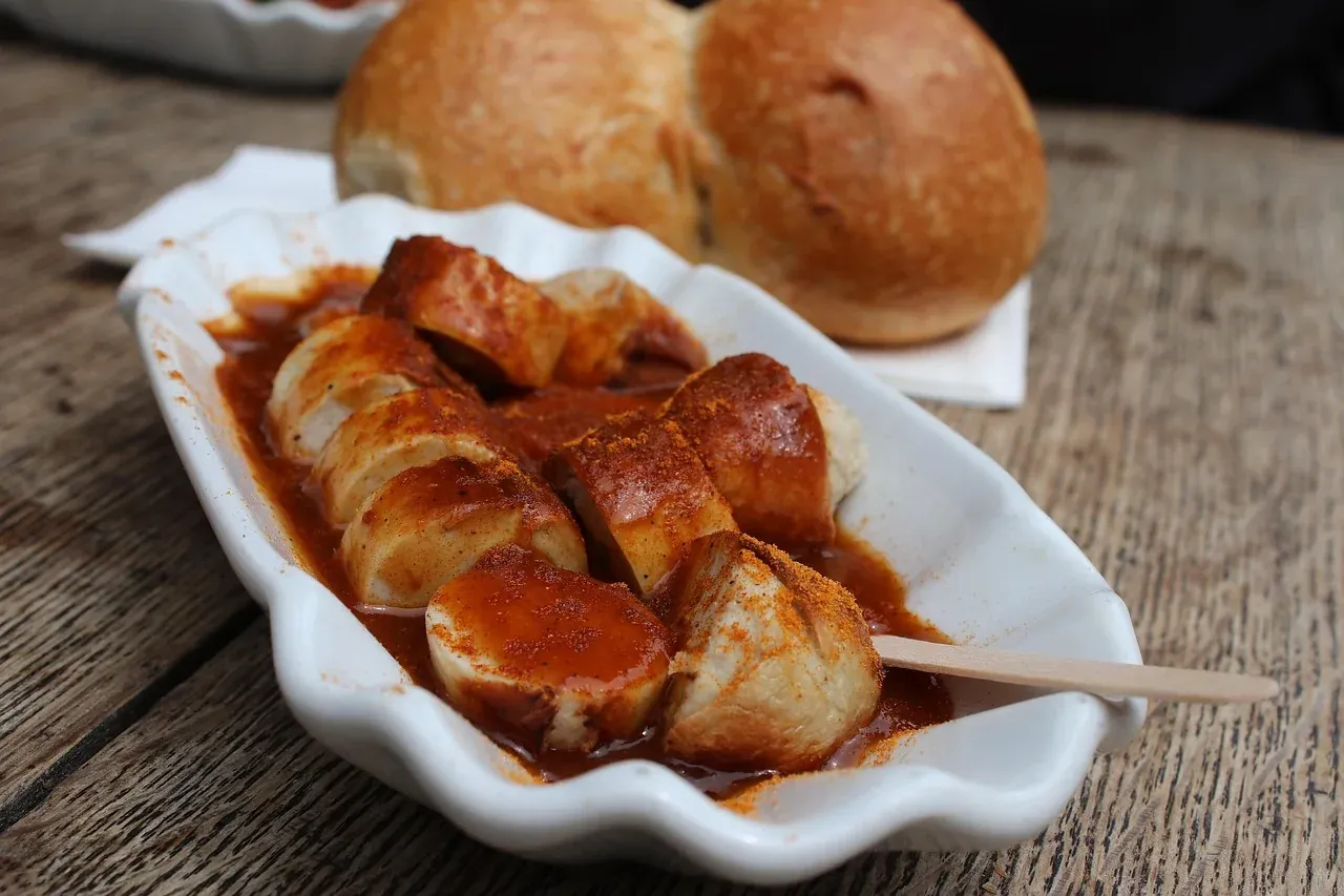 Sliced currywurst under curry sauce with bread rolls