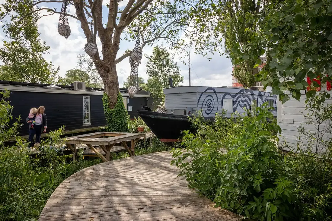 A wooden boardwalk through the gardens of De Ceuvel in Amsterdam-Noord, with converted houseboats on land