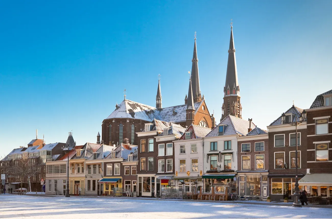 A snow-covered square in Delft's old town, with the twin neo-Gothic towers of the Maria van Jessekerk behind, Netherlands