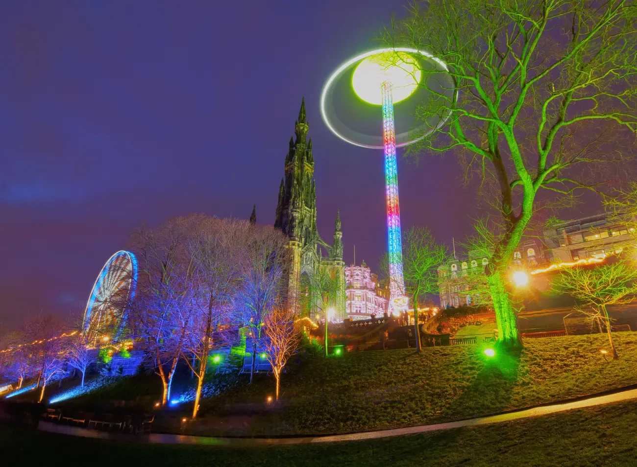 Scott Monument, a lit Star Flyer ride and illuminated trees in East Princes Street Gardens, Edinburgh, at night